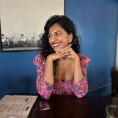 Woman with dark wavy hair, pink shirt, in a cafe